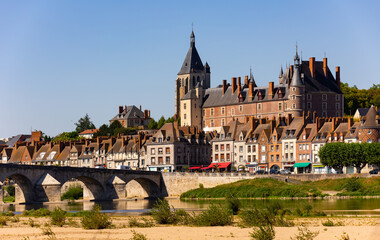 Fototapeta premium View of Gien cityscape on bank of Loire with row of townhouses along embankment, medieval renaissance castle and arched bridge across river on summer day, Loiret, France