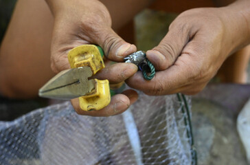 Man with pliers opens tin weights for fishing net on the table. mechanical tools.