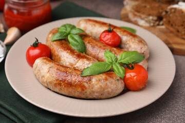Plate with tasty homemade sausages, basil leaves and tomatoes on brown textured table, closeup