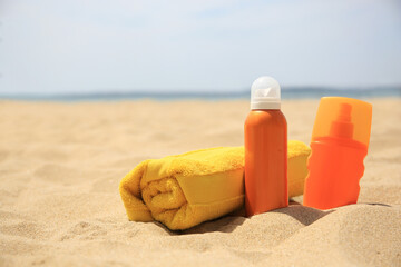 Sunscreens and rolled towel on sandy beach, space for text. Sun protection care