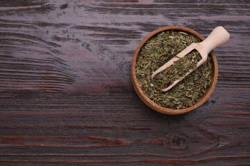 Bowl of dry tarragon and scoop on wooden table, top view. Space for text