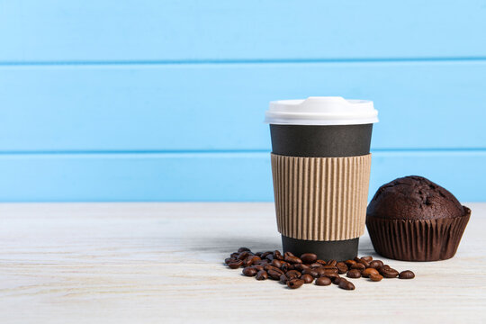 Paper cup with plastic lid, coffee beans and muffin on white wooden table, space for text. Coffee to go