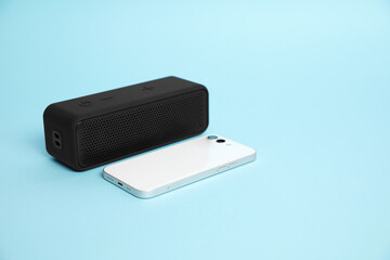 Portable bluetooth speaker and smartphone on light blue background, space for text. Audio equipment