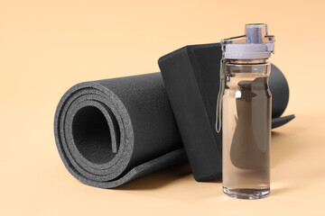 Grey exercise mat, yoga block and bottle of water on beige background