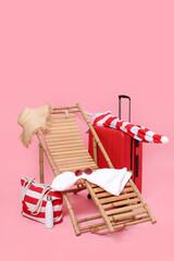 Fototapeta na wymiar Deck chair, suitcase and beach accessories on pink background