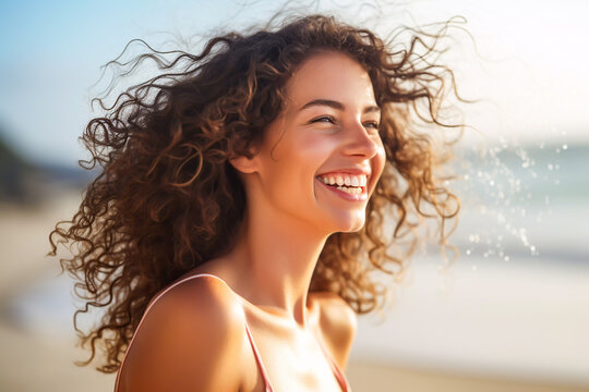 portrait of an attractive young woman with the wind in her hair smiling and having fun on the beach with the surf in the background having fun relaxing no cares or worries