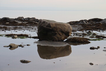 Big rock on a beach. Beach landscape in summer and low tide. Reflection of water and zen landscape. Horizon and coast.