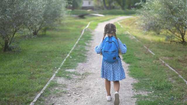 child girl with a backpack goes in the park. education learning school concept. a schoolgirl with a backpack in a dress goes along the way to school back. girl rushes to lifestyle school