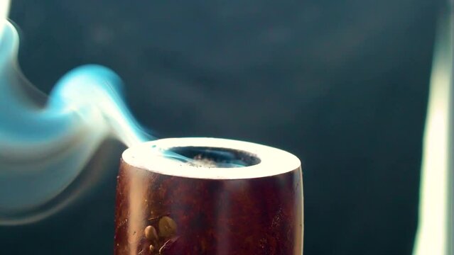 extreme close up of a old fashioned pipe top part only that vapour a thick smoke of blue colour looking like a spirit essence of something greater wooden build black back drop indoor setup