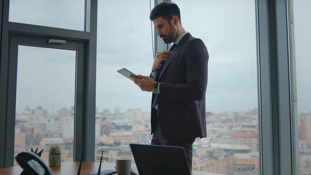 Focused manager looking tablet screen standing modern office. Man working at pad