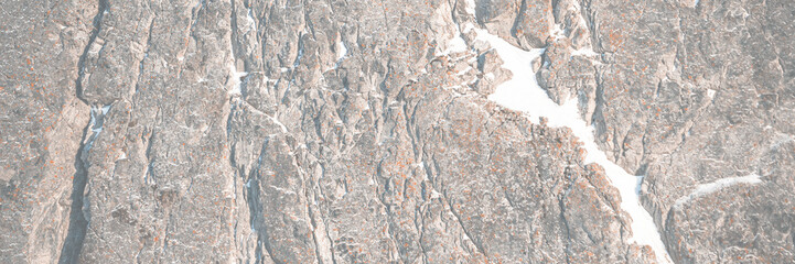 Rock texture. Snow and cracks on the surface of the cliff. Natural stone background.