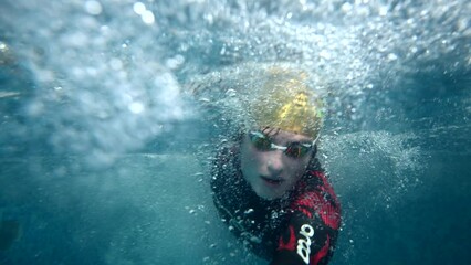 Underwater view of professional swimmer training in swimming pool, 4k 120 fps super slow motion raw video. Triathlete swim in black wetsuit 
