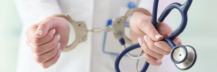 Doctor in white coat with handcuffs holds stethoscope