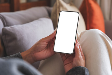 Mockup image of a woman holding mobile phone with blank desktop white screen whilesitting on a sofa...