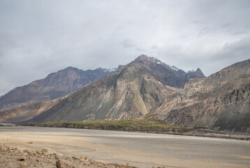 Scenic view of Himalayas and Ladakh ranges. Beautiful barren hills in Ladakh with dramatic clouds in the background.  Road side view, Shyok river , rocks and greenery in base of the mountains.
