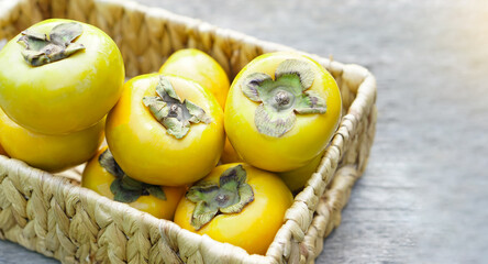 Ripe yellow sweet persimmon fruits in wicker basket. Diospyros family plants.  Concept, Agriculture crops. Seasonal fruit. Healthy eating. 