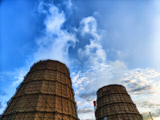 CHP cooling towers from which smoke is coming out against blue sky. A large pipe of a thermal power plant with smoke and steam on a blue sky background