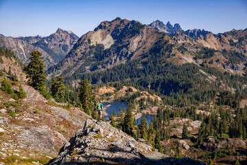 Adventurous athletic male hiker standing on top of a hill looking out at a mountain range on a beautiful sunny fall day in the Pacific Northwest.
