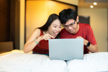 2 Asian men and women online business owners wearing a red shirt pointing at laptop Laughing, excited and happy The two were looking at a marketing project together in a hotel bedroom.