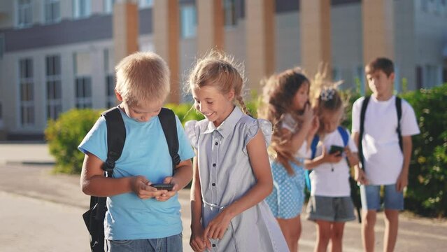 children group school children look at the smartphone video. school learning kid concept. group of kids with backpacks playing smartphone lifestyle near the school building outdoors