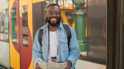 Happy Smiling young african american man in glasses with map at european terminal train station...