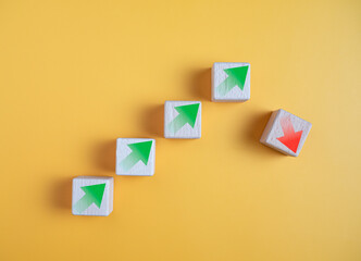 Green arrow and red arrow on wooden block represents economy trending downwards on yellow...