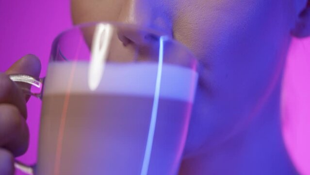 Close up of a pretty woman while enjoying a vegan freshly brewed coffee latte macciato or cappuccino in the morning for breakfast and smiling happily in front of purple background in slow motion	