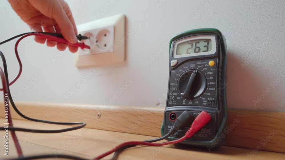 Poster man measuring the voltage from a wall socket with a digital multimeter