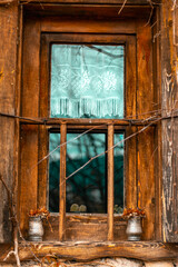Window of old wooden house with white curtains with flowers in  front.