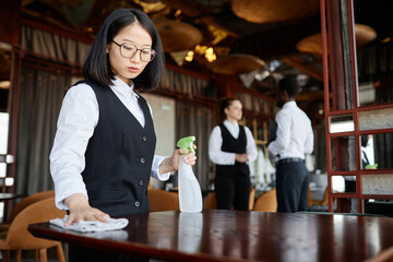 Waist up portrait of young Asian woman as server wiping tables in luxury restaurant preparing for opening, copy space