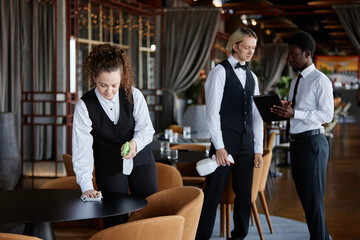 Group of servers in classic uniform preparing luxury restaurant for opening and wiping tables, copy...
