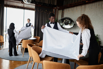 Group of elegant servers wearing classic uniforms preparing luxury restaurant for grand opening, copy space