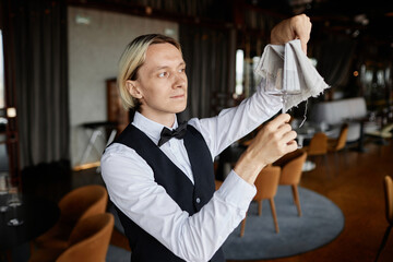 Waist up portrait of classic server with bowtie polishing glasses in luxury restaurant, copy space