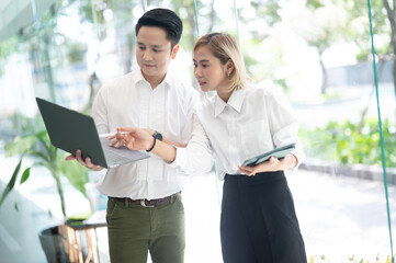 business man and a business woman, engage in a discussion as they read a financial report together. Young business professionals working together in a modern finance company.