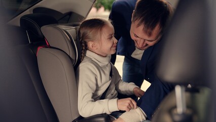 Cute little girl waits while father unlocks safety belt of child seat in car