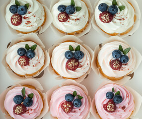 Set of cupcakes with pink and white whipped cream tops decorated with blueberries and raspberries covered with gold in a white gift box. Tasty Valentine's Day present. Flat lay