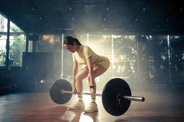 Young woman doing deadlift with heavy bar in gym, strong female athlete with muscular body lifting weights, exercising with barbell. - obrazy, fototapety, plakaty