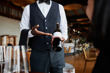 Close up of waiter presenting bottle of red wine in luxury restaurant, copy space