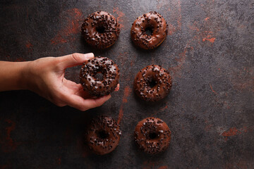 Chocolate donuts and hand on dark gray background, top view