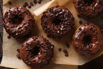 Chocolate donuts on paper on wooden background, top view