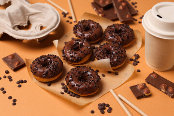 Chocolate donuts, chocolate and paper cup on orange background