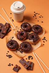 Chocolate donuts, chocolate and paper cup on orange background