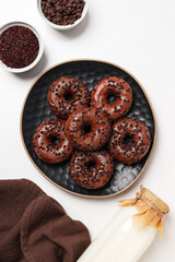 Chocolate donuts on plate, bottle with milk and bowls on white background, top view