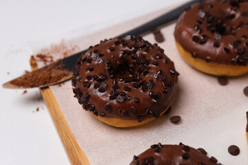 Chocolate donuts on kitchen board and knife on white background, close up