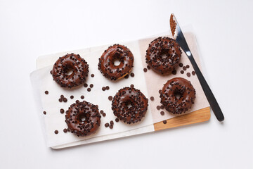 Chocolate donuts on kitchen board and knife on white background, top view