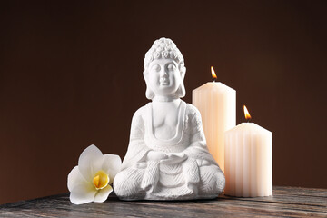 Buddha statue, flower and candles on brown background