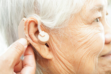 Doctor install hearing aid on senior patient ear to reduce hearing loss problem. - obrazy, fototapety, plakaty