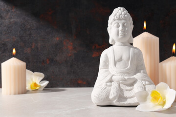 Buddha statue, candles and flowers on dark background, space for text