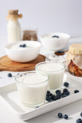 Bowls with yogurt, berries, bottle with milk and jars on white background