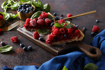 Berry pie on kitchen board and berries in bowls on a dark gray background